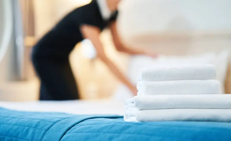 Cameriera sistema letto, asciugamani bianchi in primo piano.