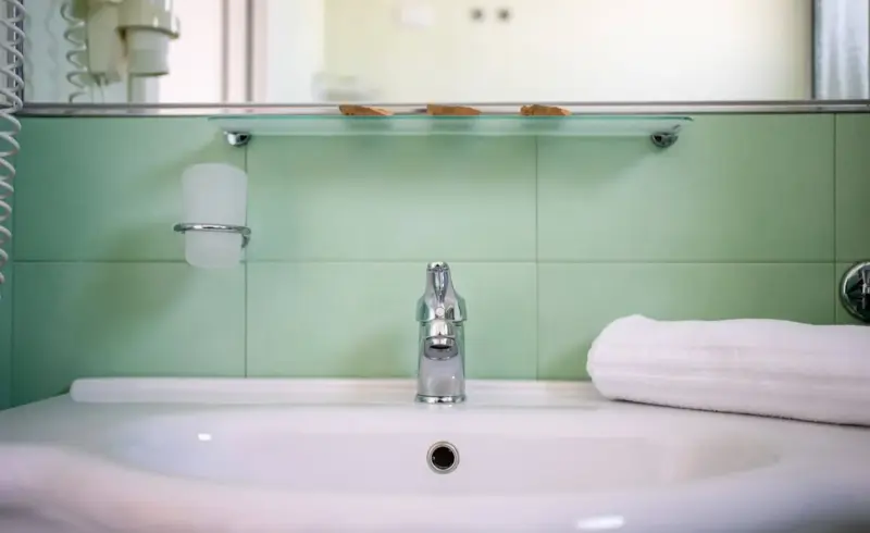Lavabo moderno con piastrelle verdi e asciugamano bianco.