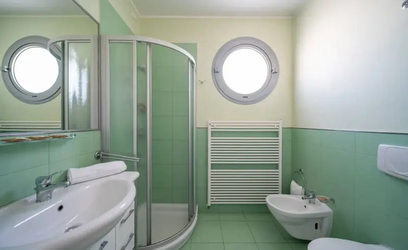 Bagno moderno con piastrelle verdi e doccia circolare.