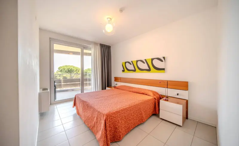 Camera da letto luminosa con balcone e letto matrimoniale.