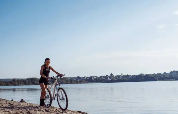 Persona in bicicletta vicino a un lago soleggiato.