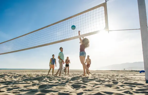 Persone giocano a beach volley sulla spiaggia soleggiata.