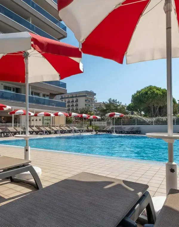 Piscina con lettini e ombrelloni rossi e bianchi.