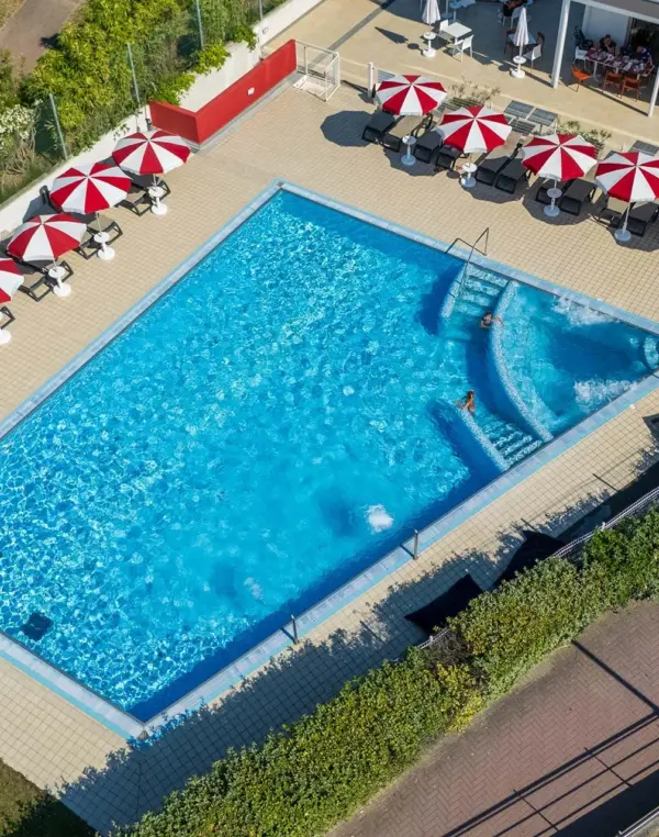 Piscina esterna con ombrelloni rossi e bianchi.