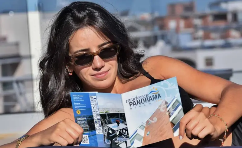 Donna legge brochure "Residence Panorama Beach" in terrazza.