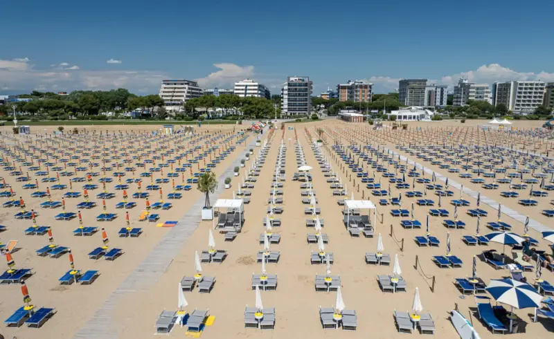 Spiaggia con numerosi lettini e ombrelloni sotto cielo sereno.