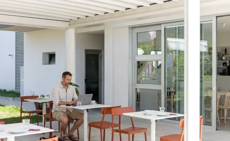 Uomo lavora al computer in terrazza di un caffè.