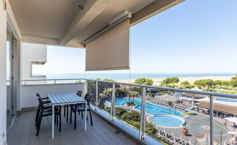 Terrazza con vista su piscina e spiaggia, giornata soleggiata.