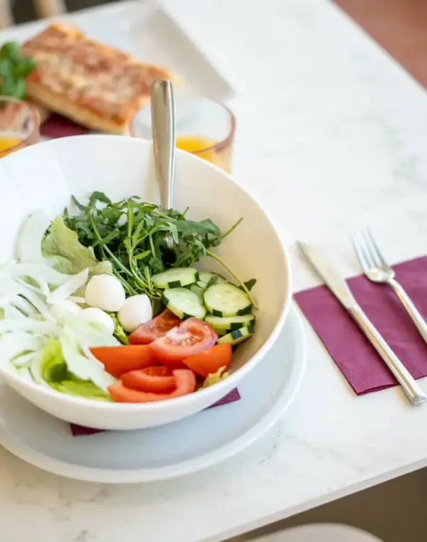 Insalata fresca in ciotola bianca, tavolo con sandwich.