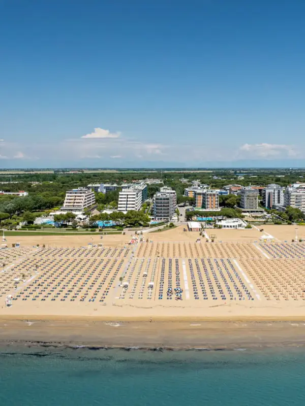 Spiaggia affollata con ombrelloni e città sullo sfondo.