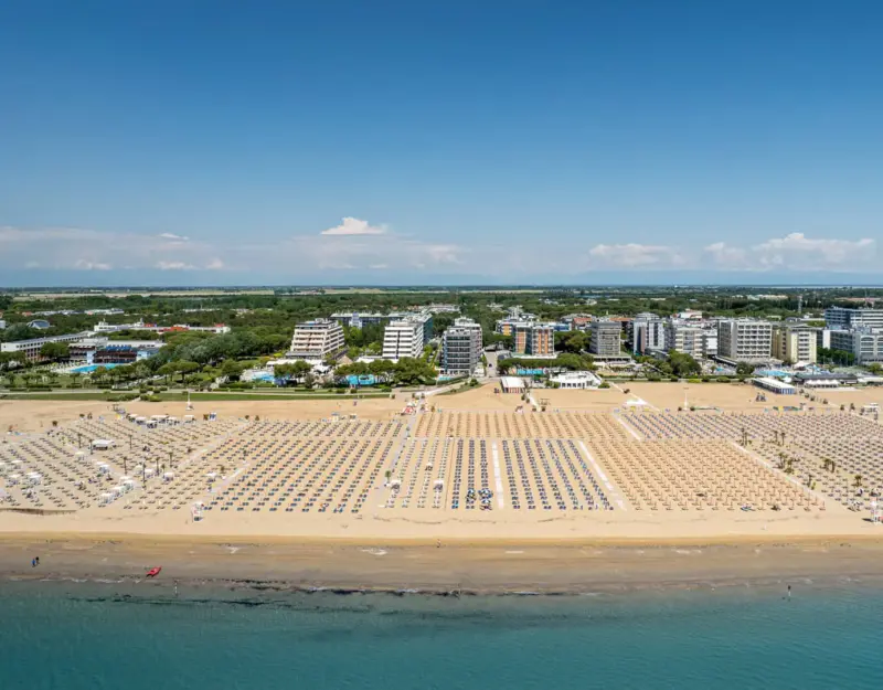 Spiaggia affollata con ombrelloni e città sullo sfondo.